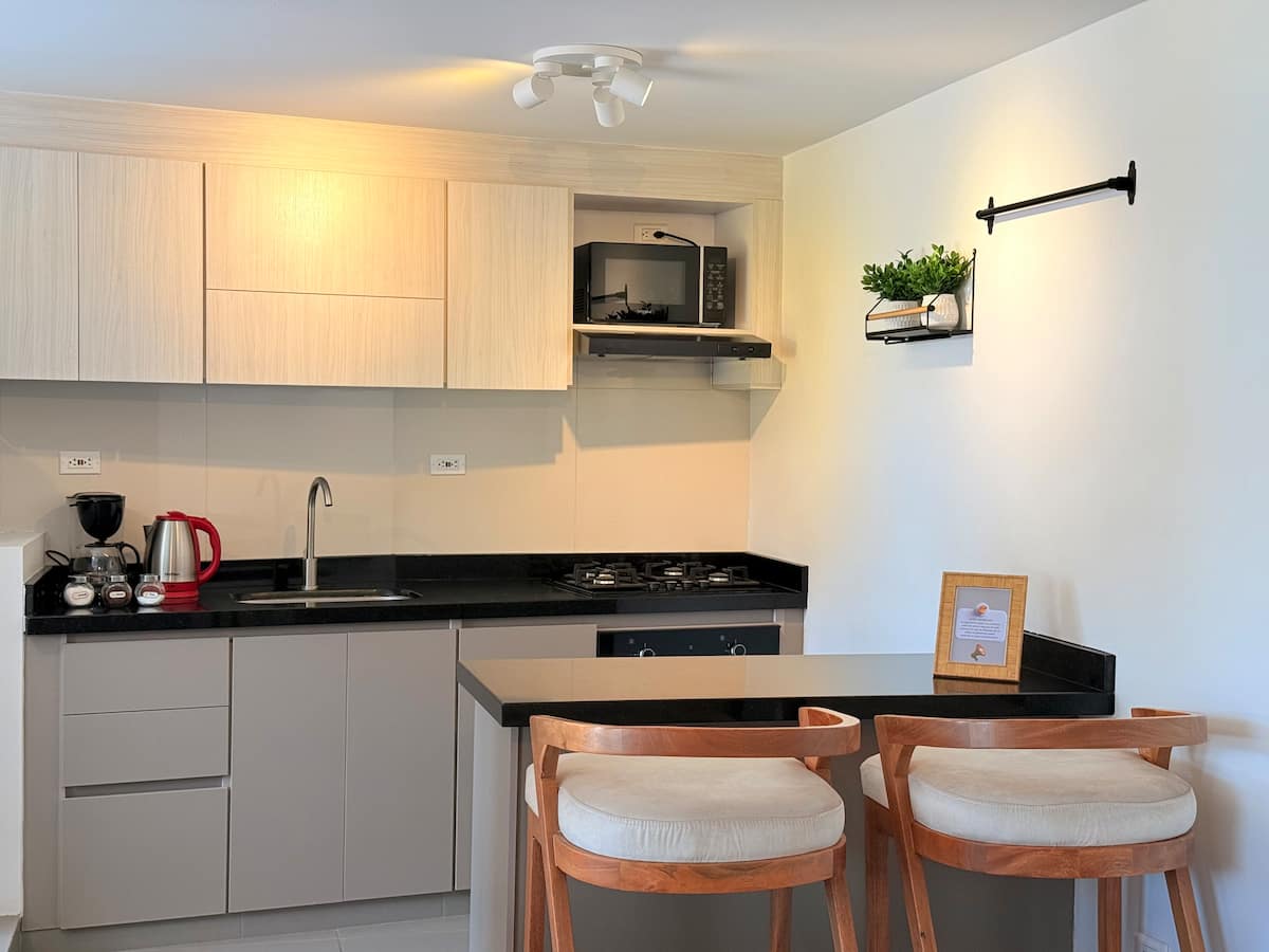 Cocina integral con barra en granito negro, dos taburetes de madera y microondas