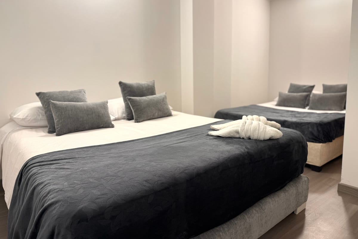 Habitación con dos camas dobles, cojines grises y toallas dobladas sobre la cama