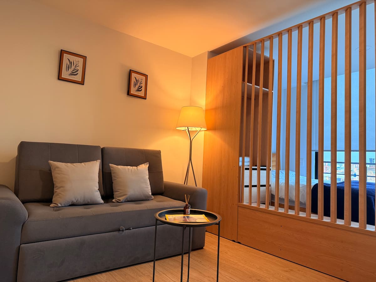 Sofá cama gris con lámpara de pie y biombo de listones que separa el dormitorio