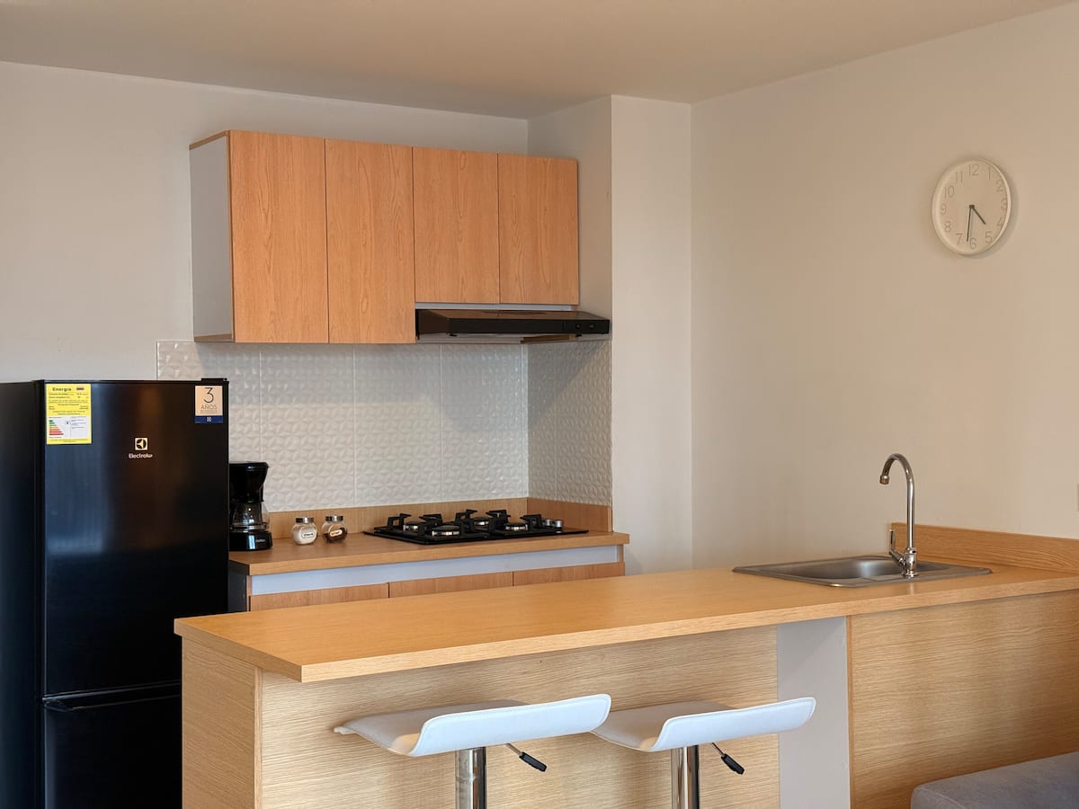 Cocina con barra de madera, taburetes blancos, estufa a gas y nevera negra