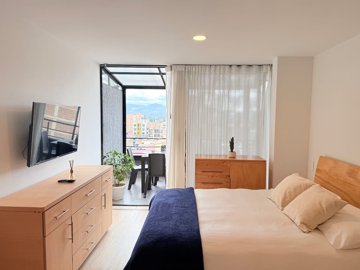 Habitación con cama doble, televisor, cómodas de madera y salida a la terraza cubierta