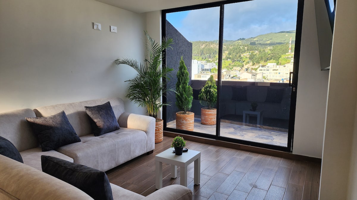 Sala con sofás beige y ventanal corredizo hacia la terraza con vista a las montañas
